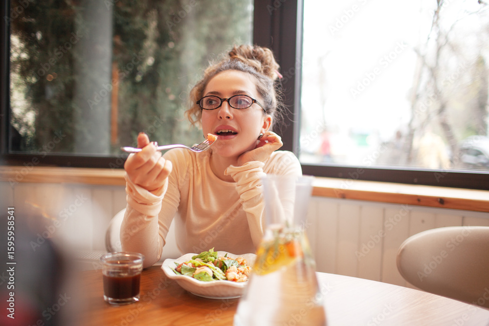 A young girl is siting in a cafe and eating a healthy salad and drinking coffee A young girl is siting in a cafe and eating a healthy salad and drinking coffee