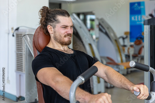 Young good looking physical trainer shows how to build upper part body by pulling up an equipment in a fitness room. A muscular sport man taking an exercise with fitness equipment to build his body.