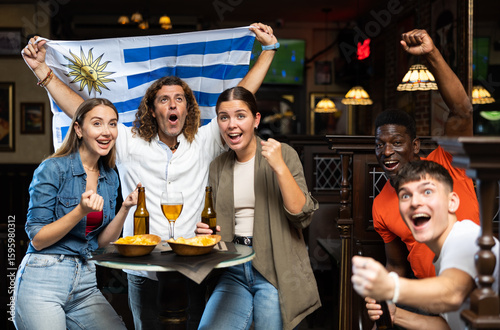 Fans with the flag of Uruguay celebrate the victory of their favorite team in a beer bar