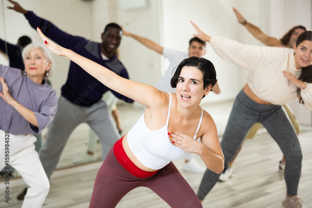 Obraz premium Happy young woman practising modern dance moves with other people in dance studio