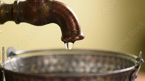 Close-up of a Copper Faucet with Water Dropping into a Metal Bucket, Showcasing Water Conservation.