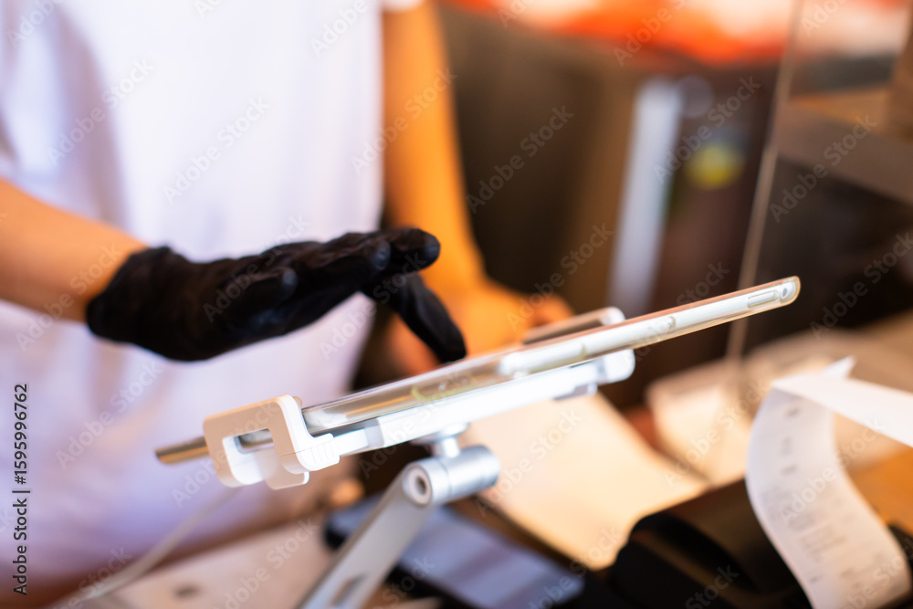 Fototapeta premium Selective focus to edge of tablet with blurry hand of Cashier staff to receive orders from customers at counter service in cafe.