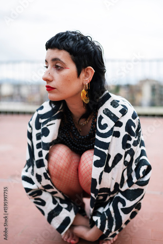 Serene informal female in stylish clothes sitting on hunkers on roof of bundling and looking away
