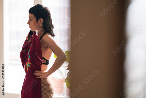 Side view contemplative informal female in bra trying purple dress while standing in light room