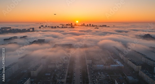 Cityscape view of buildings emerging from a sea of fog under a bright sunrise, with a plane visible in the sky.