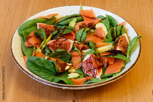 Healthy salad with smoked salmon, spinach, avocado and fig on wooden table
