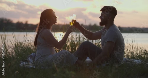 Date at the nature. Young couple drinking wine on picnic in the sunset.