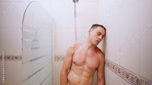Exhausted man sleeping while taking a shower in bathroom