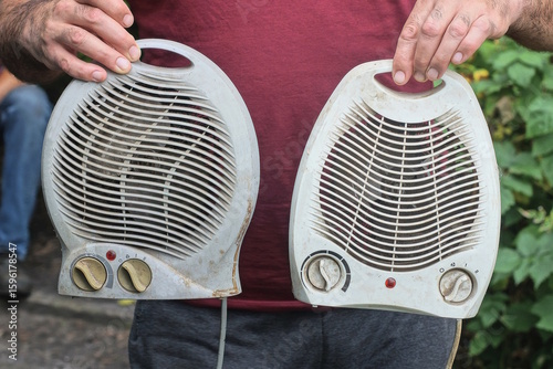 Fototapeta Naklejka Na Ścianę i Meble -  man holding two gray white electric heaters on summer street