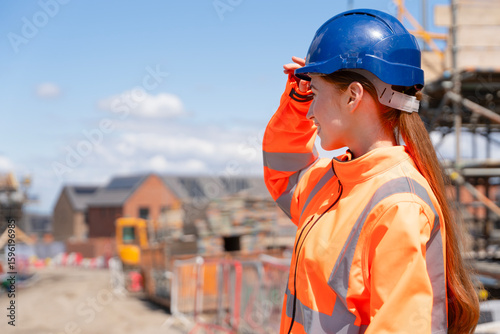 Portrait of young woman construction worker in safety gear standing confidently on building site