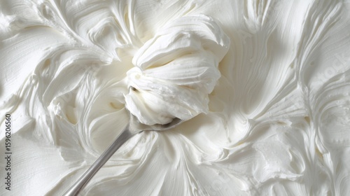 Close-up of a spoon with a generous amount of whipped cream on it. the whipped cream is white and fluffy, and it appears to be smooth and creamy. the spoon is silver and has a curved handle.