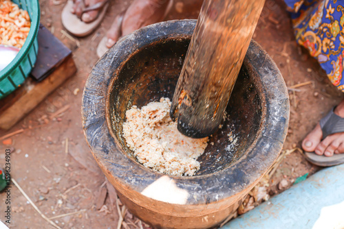 Dried shrimp are crushed with both hands using a large wooden mortar and pestle.