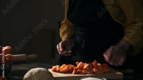 A Close-Up Shot of a Woman's Hands Skillfully Slicing Fresh, Ripe Apricots on a Wooden Cutting Board, Preparing Delicious Fruit for a Homemade Pie in a Warm, Rustic Kitchen Setting.