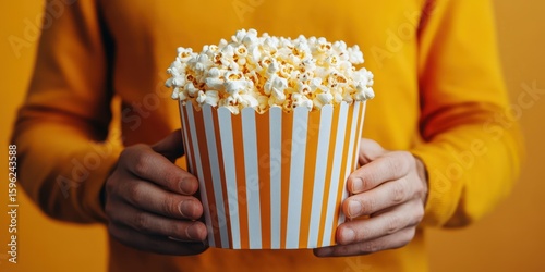 Brightly colored popcorn bucket held by a person in a yellow sweater against a matching backdrop