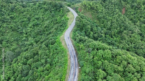 Aerial view of car driving on country road in forest. Cinematic drone shot flying over country road with curved in the mountain.	