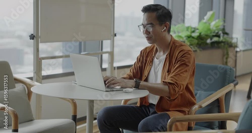 Senior Asian businessman wearing headset celebrates success during online meeting in modern co-working space. Remote work and business communication concept.
