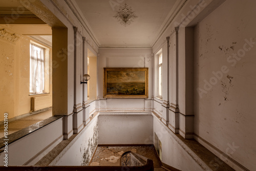 Abandoned elegant staircase with peeling walls and classic painting in a decaying historic building interior