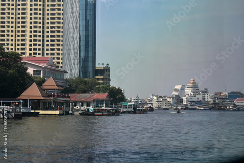 Fototapeta Naklejka Na Ścianę i Meble -  River view of Bangkok city with traditional Thai houses and modern skyscrapers contrasting against the sky.