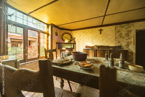 Abandoned rustic farmhouse dining room with dusty tableware, old bottles, and vintage decor illuminated by natural light through large windows