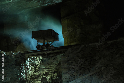 Abandoned mining cart on old rail tracks inside a dark, mysterious underground cave with atmospheric blue light and stone walls