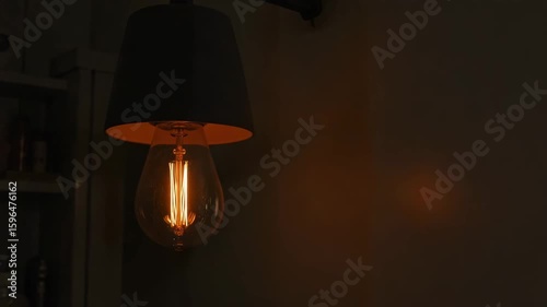 A vintage incandescent light bulb flickers while hanging from a lampshade indoors.