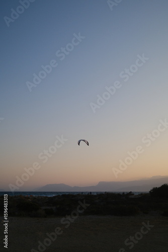 Fototapeta Naklejka Na Ścianę i Meble -  Several kitesurfers ride along the Turkish coastline at sunset. The silhouettes of kites contrast beautifully against the pastel evening sky. Ideal for themes of sport, freedom, beach holidays, and ac