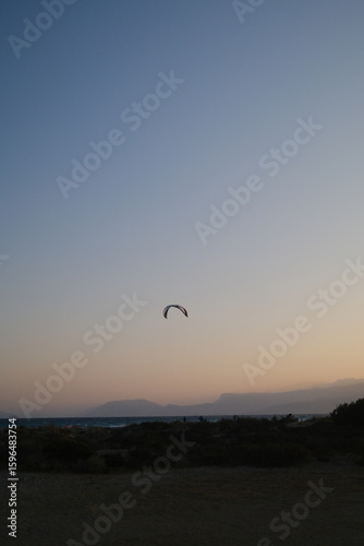 Fototapeta Naklejka Na Ścianę i Meble -  Several kitesurfers ride along the Turkish coastline at sunset. The silhouettes of kites contrast beautifully against the pastel evening sky. Ideal for themes of sport, freedom, beach holidays, and ac