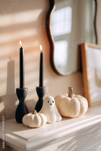 minimal halloween decor with white ghost and textured pumpkins on elegant shelf in natural light with long shadows, modern cozy autumn interior, stylish black candles and mirror, home concept