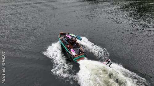 Aerial tracking shot focused on boat capturing wake surfer and lake Ullswater Lake District UK on cloudy day