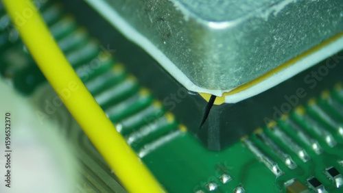 Microchip close up on green circuit board with yellow wire showing electronic chip detail and metal component in technology device
