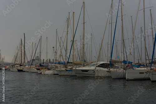 Obraz na plátně A tranquil marina scene with classic wooden boats in the foreground and numerous sailboats with tall masts docked under a clear blue sky, evoking a serene nautical mood