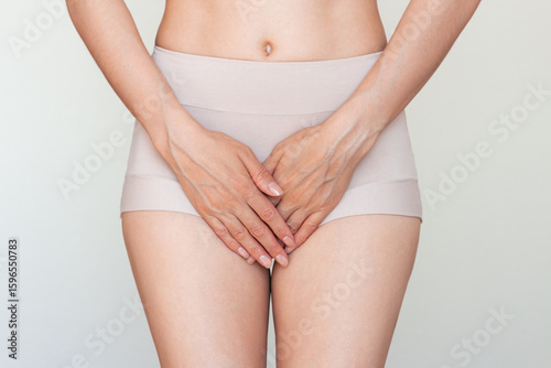 Young Caucasian woman in beige underwear holding her crotch with her hands. Suffering from severe pain, cystitis, gynecological problems, urinary incontinence. Isolated on a light background. 