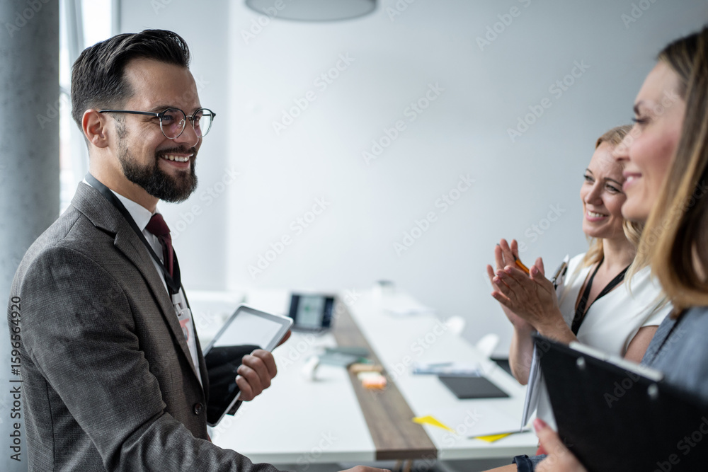 Smiling businessman holding tablet receiving applause from colleagues Smiling businessman holding tablet receiving applause from colleagues
