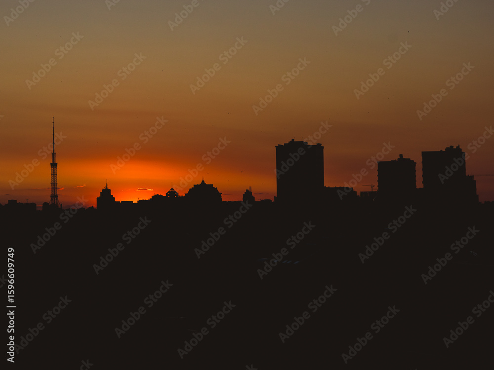 Naklejka premium Dramatic urban skyline silhouette against a fiery sunset
