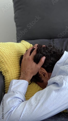 Depressed man lying on the sofa and holding his head. Sad unhappy handsome caucasian man on couch having financial troubles during quarantine or suffering from loneliness.
