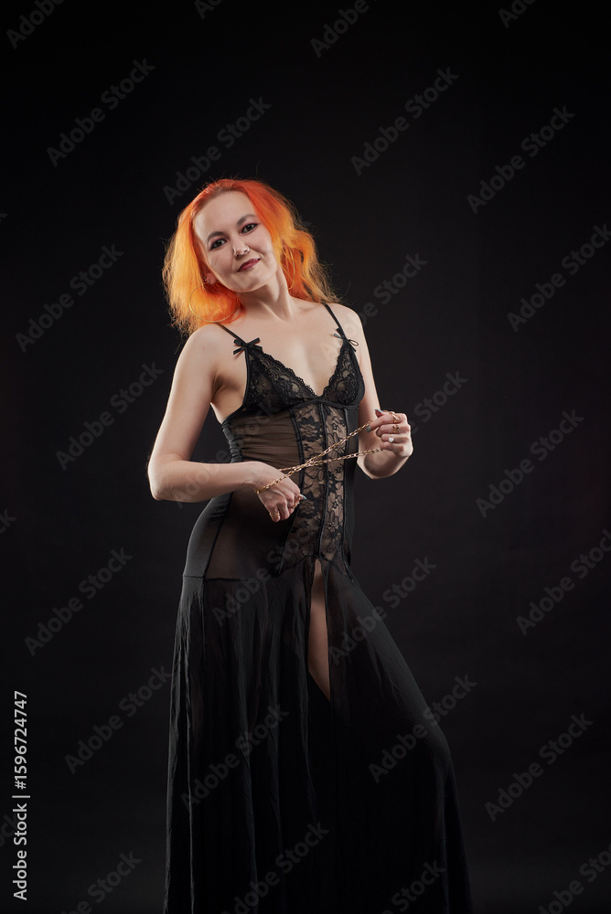 A woman in a black dress with red hair poses for the camera in a dark room. She has a beautiful figure. The girl is not wearing underwear under her dress. A woman in a black dress with red hair poses for the camera in a dark room. She has a beautiful figure. The girl is not wearing underwear under her dress.