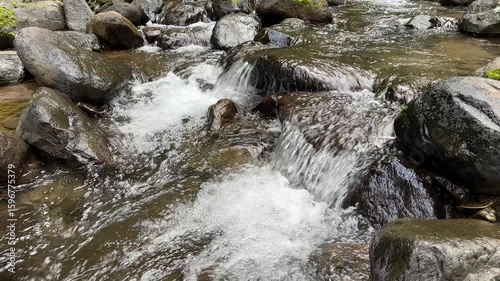 Beautiful mountain river water flows over rocks in pristine nature. A river cascading over rocks. Refreshing cold river water in a serene forest landscape with sunlight. Beautiful lansdscape. 