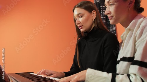 Student learns to read sheet music playing piano with teacher. Instructor fosters supportive environment for lady empowering to take on challenges slow motion