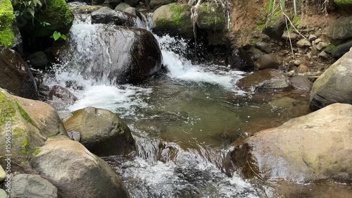Beautiful mountain river water flows over rocks in pristine nature. A river cascading over rocks. Refreshing cold river water in a serene forest landscape with sunlight. Beautiful lansdscape. 