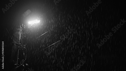 A single street lamp illuminates the torrential rain, casting dramatic shadows on a dark background. It's raining like a wall. There is a large spider web on the lantern