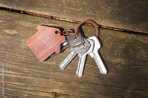 Apartment keys on table made of aged cracked wood. With wooden house shaped keychain 
