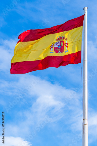 National flag of Spain flying in the wind; red and yellow national flag on blue sky background