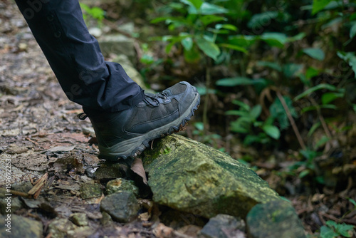 Hiking boots stepping on a mossy rock on a forest trail, a detailed, close-up shot of sturdy footwear in action, grip and stability footwear on uneven natural terrain