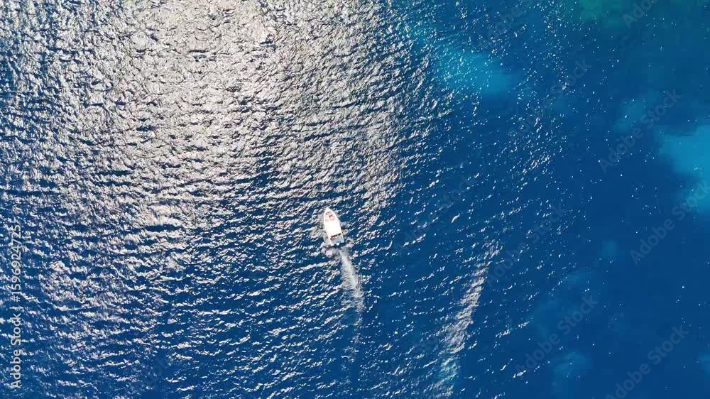 Plan de vue aérien sur un bateau en plein milieu de la mer Méditerranée vers des falaises avec une eau bleue et turquoise  