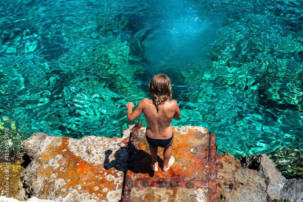 Fototapeta premium The thrill of summer captured as a young boy dives headfirst into the refreshing Ionian Sea at a hidden bay in Zante, Greece. Concept of an active holiday, youth, energy, and water sports. 