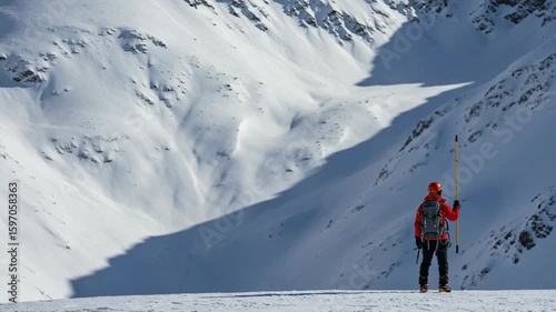 Mountain rescuer with safety equipment standing on a snowy peak. Male mountaineer or ski patroller surveying a vast winter landscape for avalanche risk.