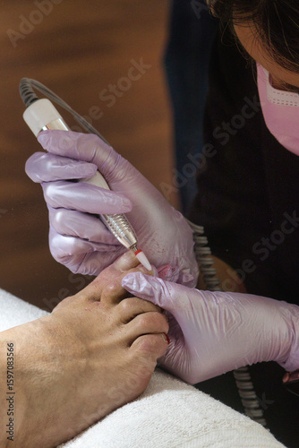 Fotografie Close-up of a pedicurist wearing pink gloves removing gel polish from toenails using an electric nail drill
