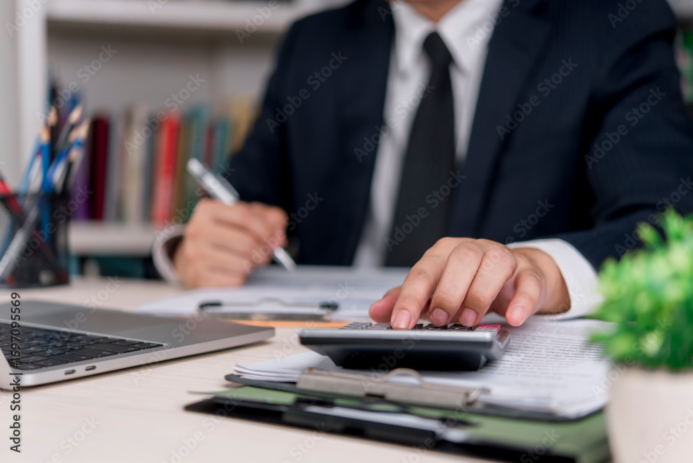 Fototapeta premium Business professional using a calculator for financial analysis and accounting. Man in suit working with documents, budget planning and tax calculation in the office.
