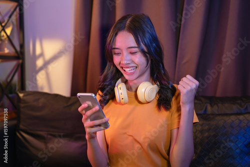 Excited Young Asian girl playing an online game on a smartphone on the sofa in the living room.
