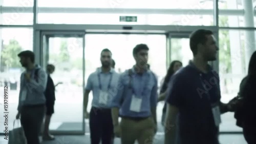 A diverse group of blurred professionals walking through the entrance of a modern event hall.